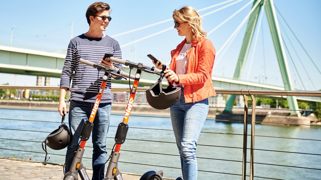 2 people talking next to a river with escooters